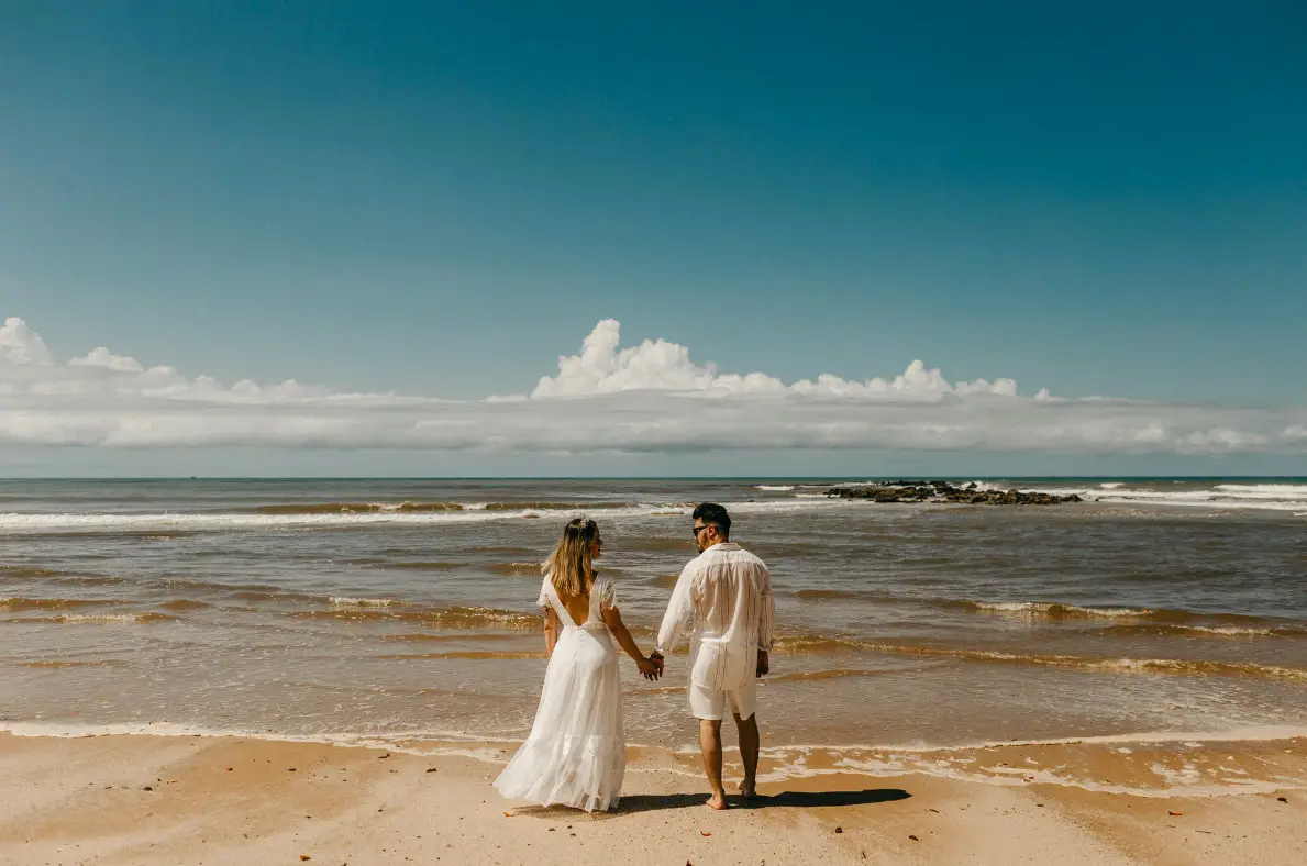 Beach wedding couple holds hands by the ocean