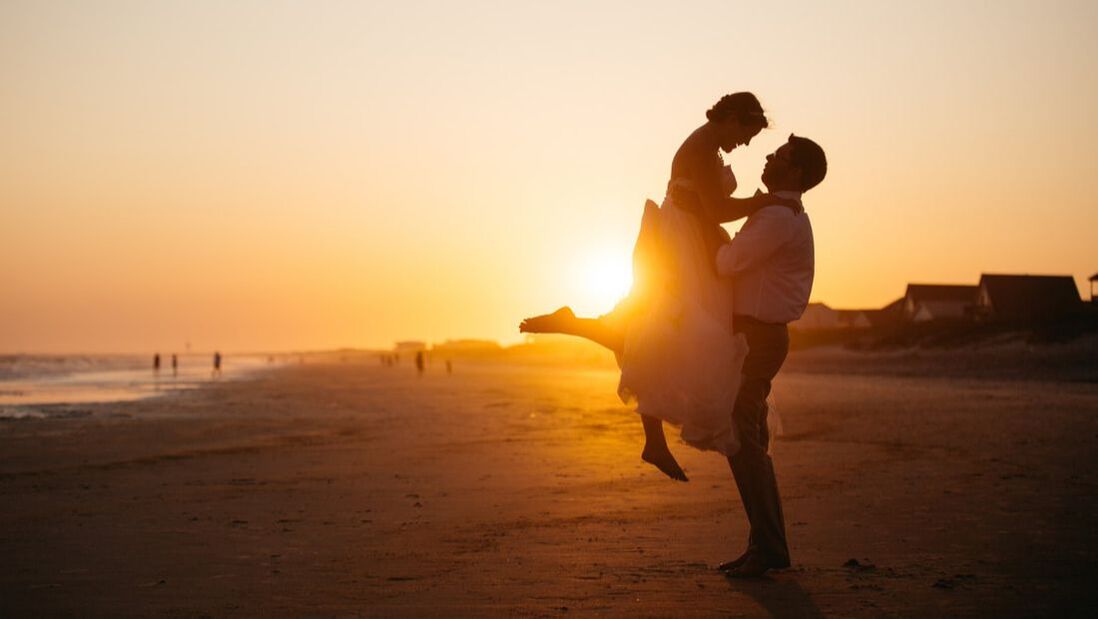 Wedding couple hugs on beach at sunset